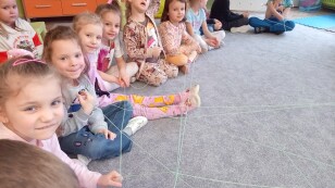 dzieci siedzą na dywanie i trzymają sznurek tworzący sieć podczas zajęć z psychologiem