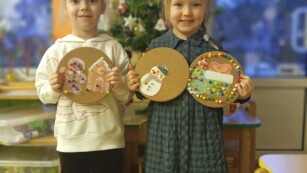 dziewczynki pokazują prace o tematyce świątecznej układanek na tabliczkach korkowych na tle kącika sensorycznego