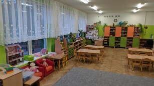 widok na salę przedszkolną ze stojącymi stolikami i kącikami zabaw