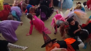 grupa dzieci z przedszkola tańczących na balu w przebraniach w pozycji jedna noga i jedna ręka na podłodze